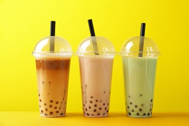 Photo of Tasty milk bubble tea in plastic cups on yellow background