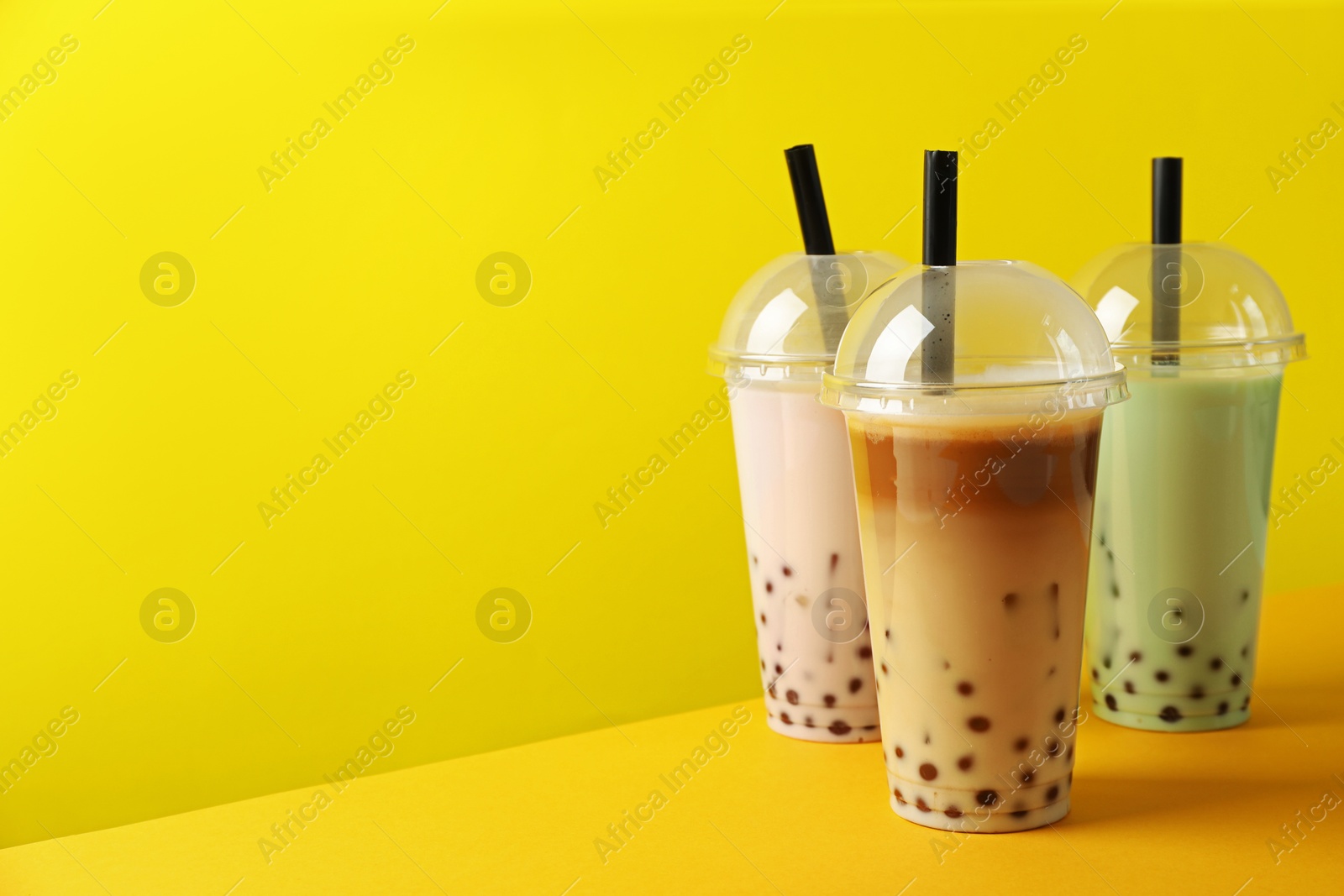 Tasty milk bubble tea in plastic cups on yellow background Photo of Tasty milk bubble tea in plastic cups on yellow background