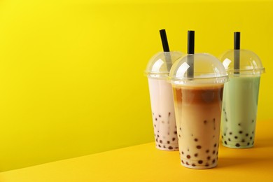 Photo of Tasty milk bubble tea in plastic cups on yellow background