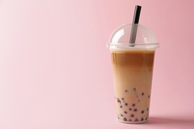 Photo of Tasty milk bubble tea in plastic cup on pink background. Space for text