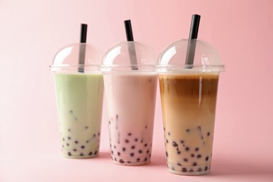 Photo of Tasty milk bubble tea in plastic cups on pink background