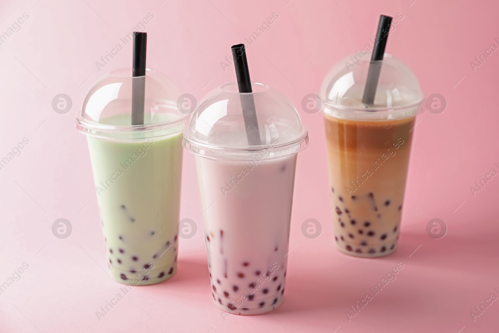 Tasty milk bubble tea in plastic cups on pink background Photo of Tasty milk bubble tea in plastic cups on pink background