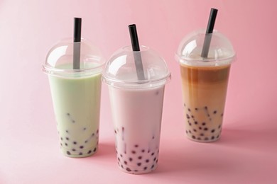 Photo of Tasty milk bubble tea in plastic cups on pink background