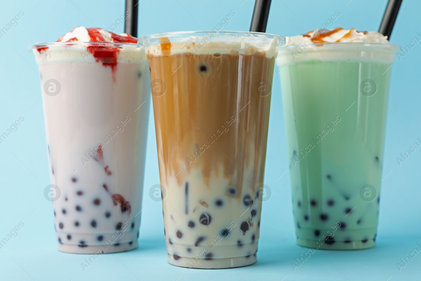 Tasty milk bubble tea in plastic cups on light blue background Photo of Tasty milk bubble tea in plastic cups on light blue background