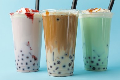 Photo of Tasty milk bubble tea in plastic cups on light blue background