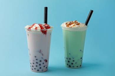 Photo of Tasty milk bubble tea in plastic cups on light blue background