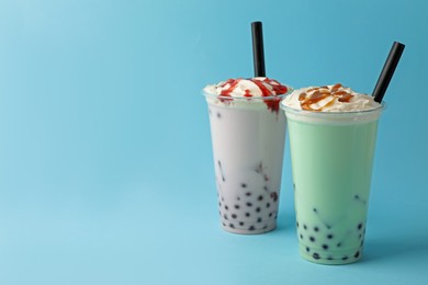 Photo of Tasty milk bubble tea in plastic cups on light blue background. Space for text