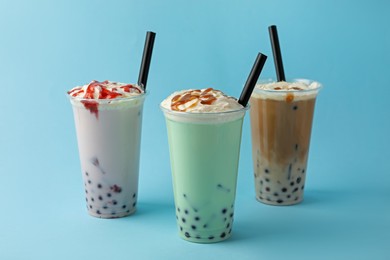 Photo of Tasty milk bubble tea in plastic cups on light blue background