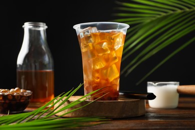 Photo of Tasty iced bubble tea and ingredients on wooden table