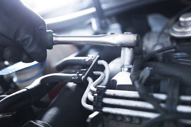 Photo of Auto parts. Professional mechanic with torque wrench fixing car indoors, closeup