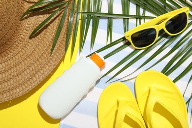 Photo of Beach towel, straw hat, flip flops, sunscreen product, sunglasses and palm leaf on yellow background, flat lay