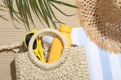 Photo of Beach towel, straw hat, bag, sunscreen product, sunglasses and palm leaf on sand outdoors, flat lay