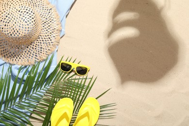 Photo of Beach towel, straw hat, sunglasses, flip flops and palm leaves on sand outdoors, flat lay. Space for text