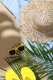 Photo of Beach towel, straw hat, sunglasses, flip flops and palm leaves on sand outdoors, flat lay