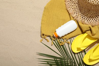 Photo of Beach towel, straw hat, flip flops, sunscreen product and palm leaf on sand outdoors, flat lay. Space for text