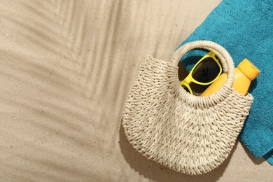 Photo of Beach towel, straw bag, sunscreen product and sunglasses on sand outdoors, flat lay. Space for text