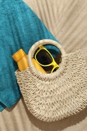 Photo of Beach towel, straw bag, sunscreen product and sunglasses on sand outdoors, flat lay