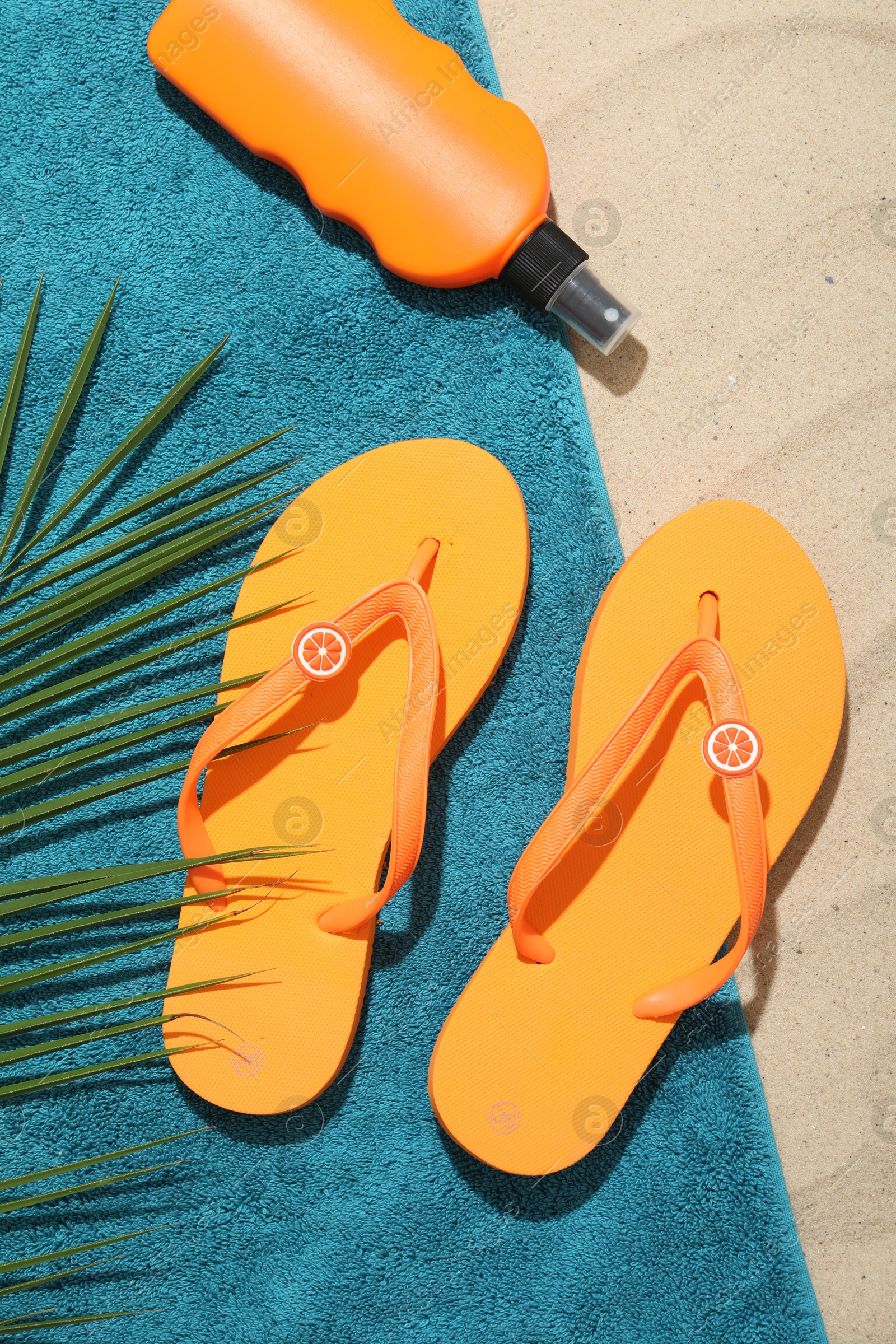 Beach towel, flip flops, sunscreen product and palm leaf on sand outdoors, flat lay Photo of Beach towel, flip flops, sunscreen product and palm leaf on sand outdoors, flat lay