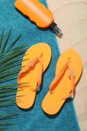 Photo of Beach towel, flip flops, sunscreen product and palm leaf on sand outdoors, flat lay