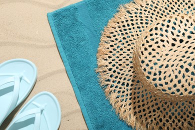 Photo of Beach towel, flip flops and straw hat on sand outdoors, flat lay