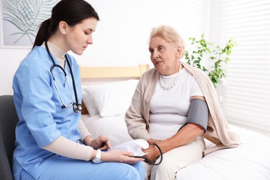 Photo of Nurse measuring patient's blood pressure indoors. Home health care service