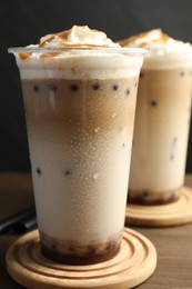 Photo of Tasty milk bubble tea in plastic cups on wooden table, closeup