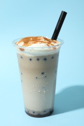 Photo of Tasty milk bubble tea in plastic cup on light blue background