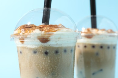 Photo of Tasty milk bubble tea in plastic cups on light blue background, closeup
