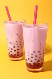 Photo of Tasty milk bubble tea in glasses on orange background, closeup