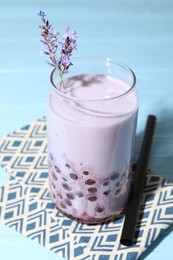 Photo of Tasty milk bubble tea in glass and lavender flowers on light blue wooden table, closeup