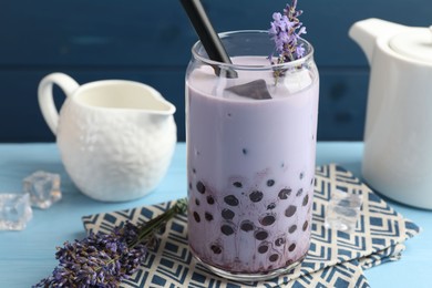 Photo of Tasty milk bubble tea in glass and lavender flowers on light blue wooden table, closeup