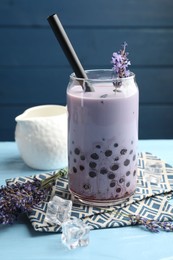 Photo of Tasty milk bubble tea in glass and lavender flowers on light blue wooden table, closeup