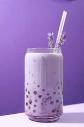 Photo of Tasty milk bubble tea in glass and lavender flowers on white table against purple background