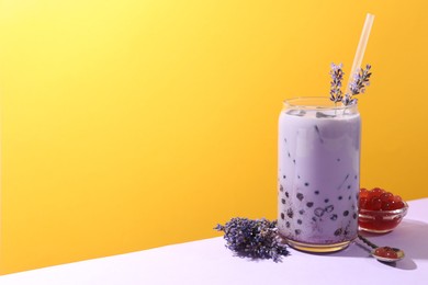 Photo of Tasty milk bubble tea in glass and lavender flowers on white table against orange background, space for text