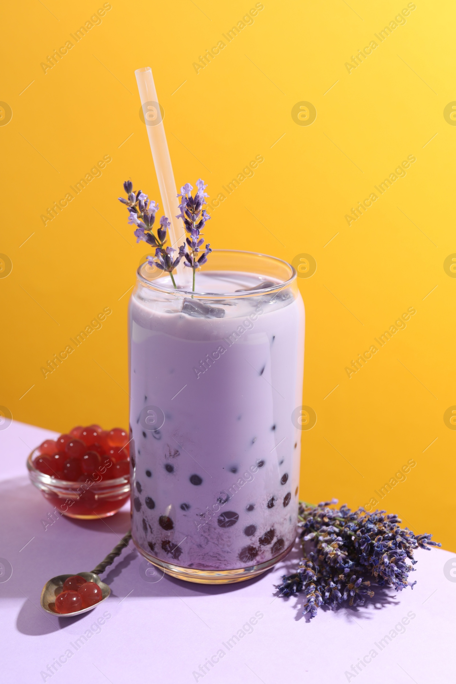 Tasty milk bubble tea in glass on white table against orange background Photo of Tasty milk bubble tea in glass on white table against orange background