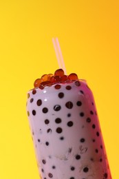 Photo of Tasty milk bubble tea in glass on yellow background, closeup