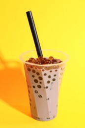 Photo of Tasty milk bubble tea in glass on yellow background