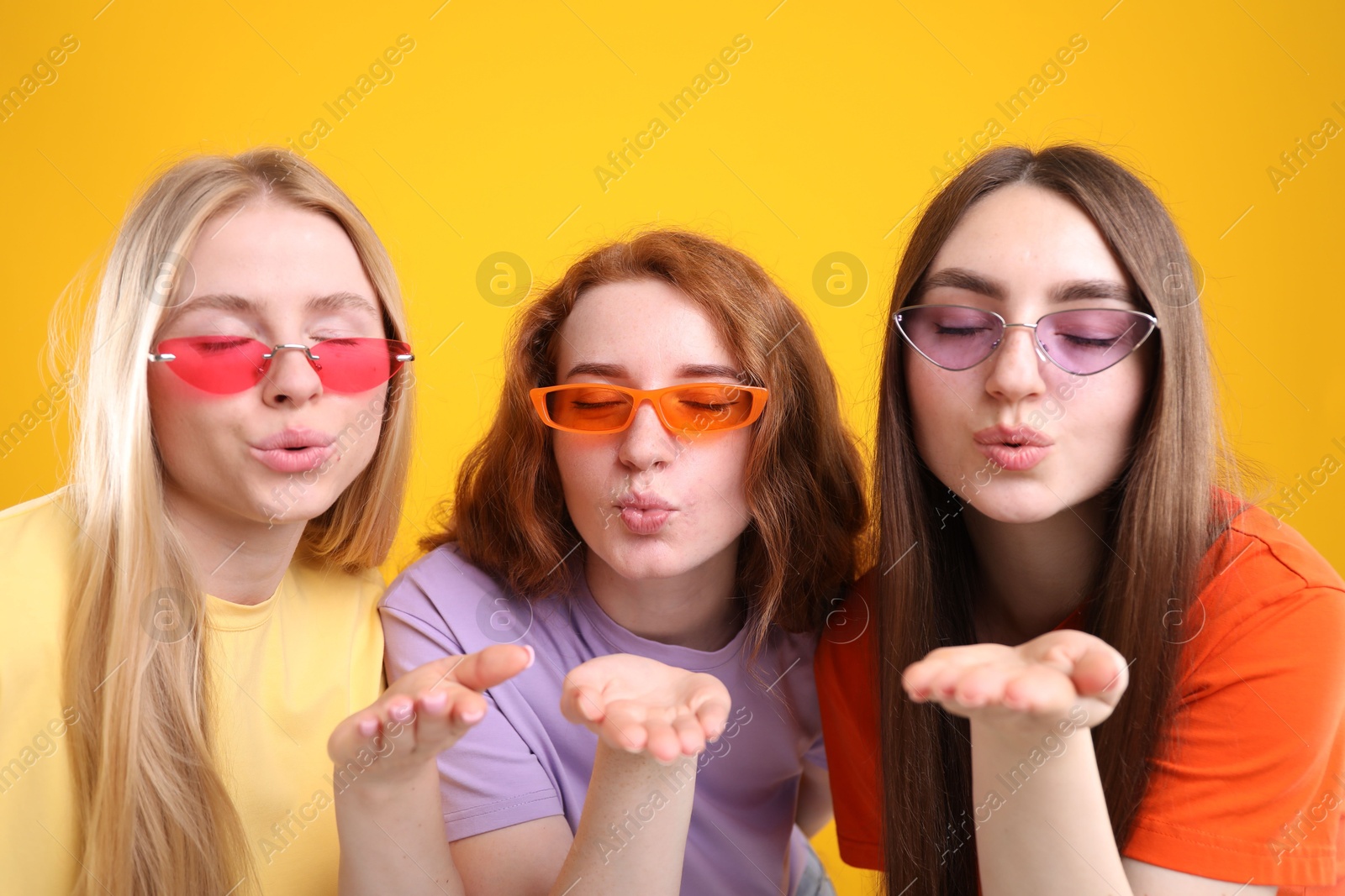 Beautiful women with different hair colors blowing kisses on orange background Photo of Beautiful women with different hair colors blowing kisses on orange background