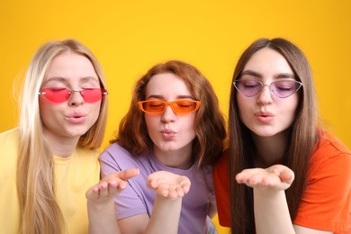 Photo of Beautiful women with different hair colors blowing kisses on orange background