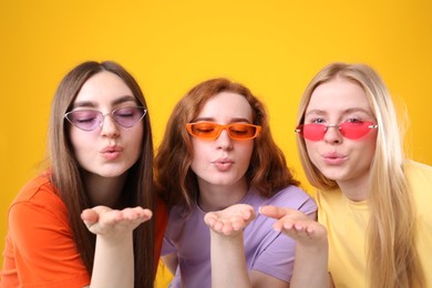 Photo of Beautiful women with different hair colors blowing kisses on orange background