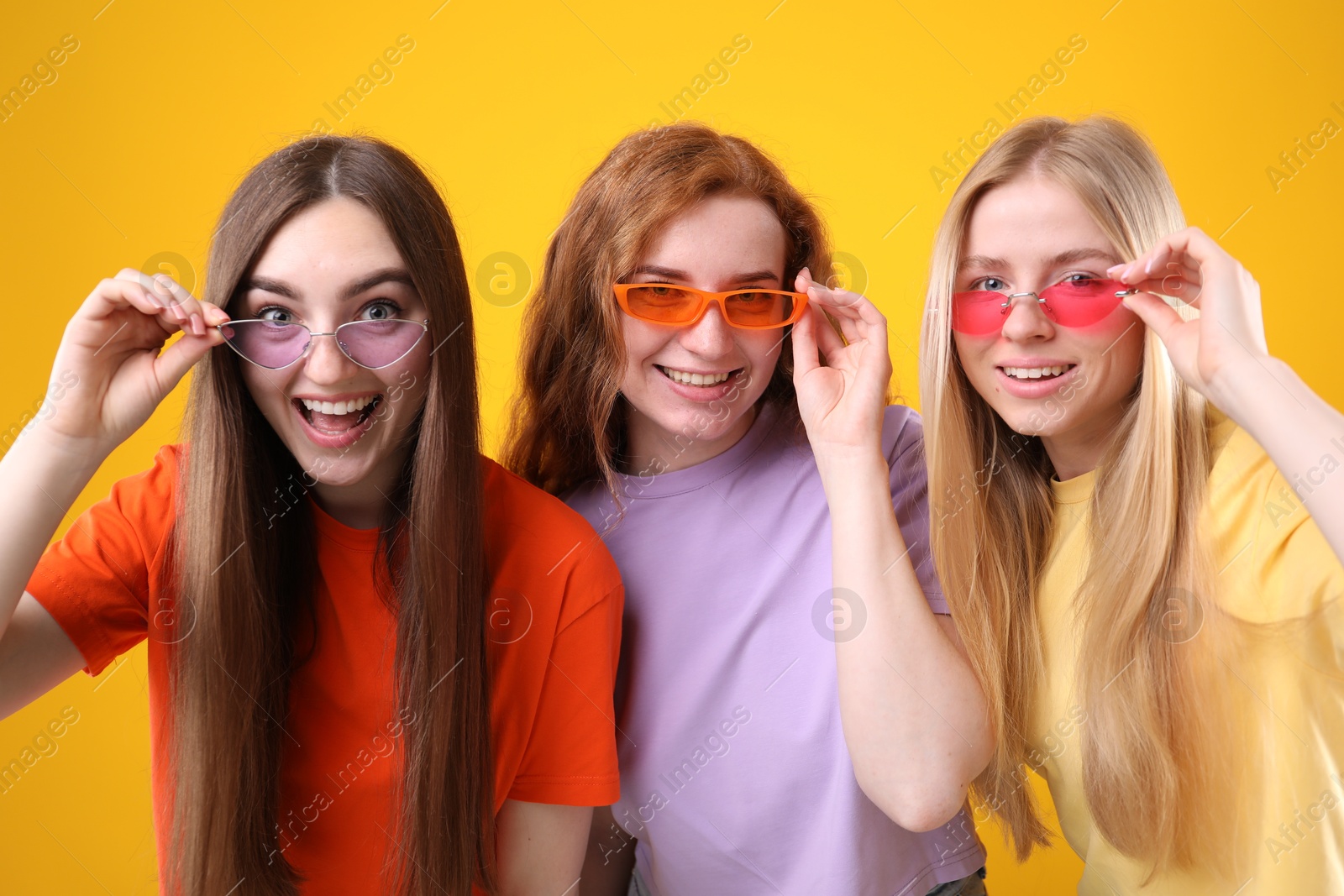 Beautiful women with different hair colors wearing stylish sunglasses on orange background Photo of Beautiful women with different hair colors wearing stylish sunglasses on orange background