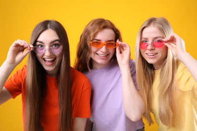 Photo of Beautiful women with different hair colors wearing stylish sunglasses on orange background