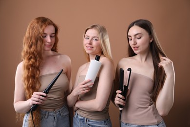 Photo of Beautiful women with different hair colors holding curling iron, shampoo and straightener on dark beige background