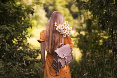 Photo of Beautiful woman with bouquet of wildflowers and backpack in forest, back view