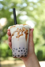 Photo of Woman with tasty milk bubble tea in plastic cup outdoors, closeup