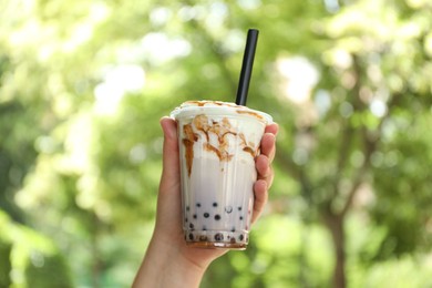 Photo of Woman with tasty milk bubble tea in plastic cup outdoors, closeup