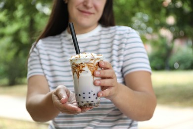 Photo of Woman with tasty milk bubble tea in plastic cup outdoors, closeup
