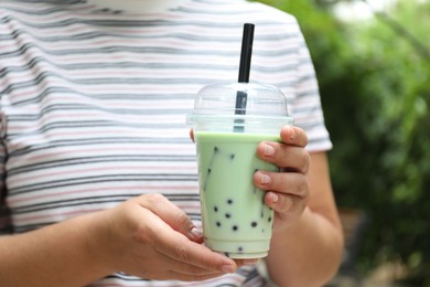 Photo of Woman with tasty milk bubble tea in plastic cup outdoors, closeup