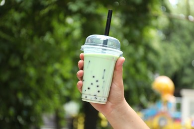Photo of Woman with tasty milk bubble tea in plastic cup outdoors, closeup