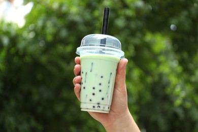 Photo of Woman with tasty milk bubble tea in plastic cup outdoors, closeup